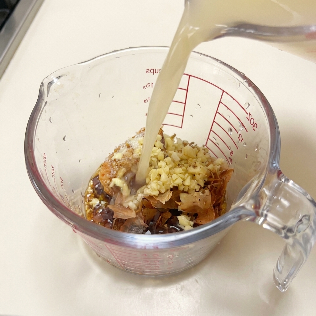Brodo di maiale caldo e opaco versato in un misurino con miso, aglio e scaglie di bonito.
