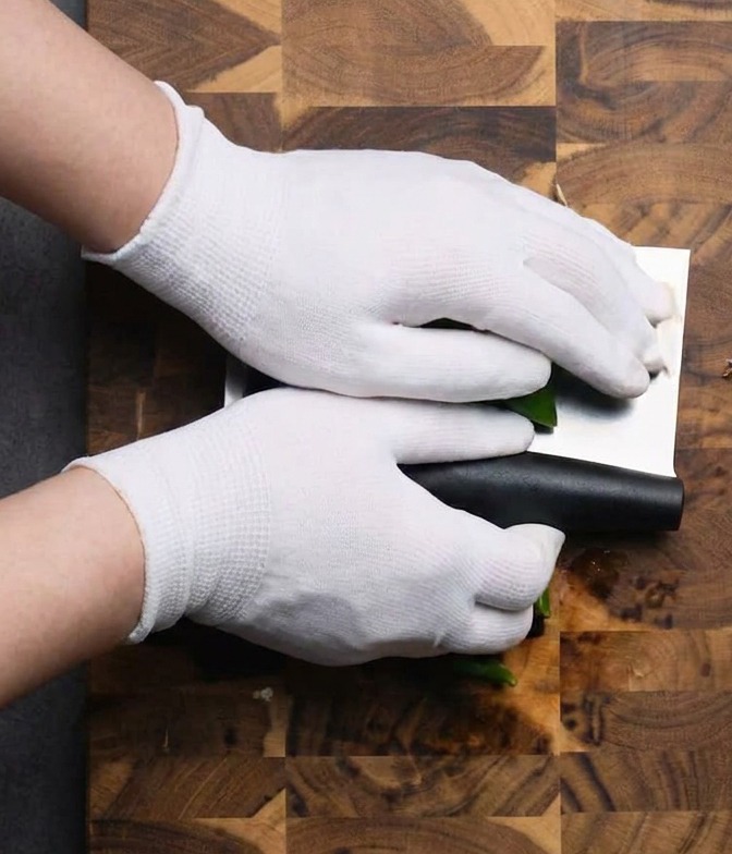 Mani che usano una mannaia per tritare i peperoncini verdi su un tagliere di legno.