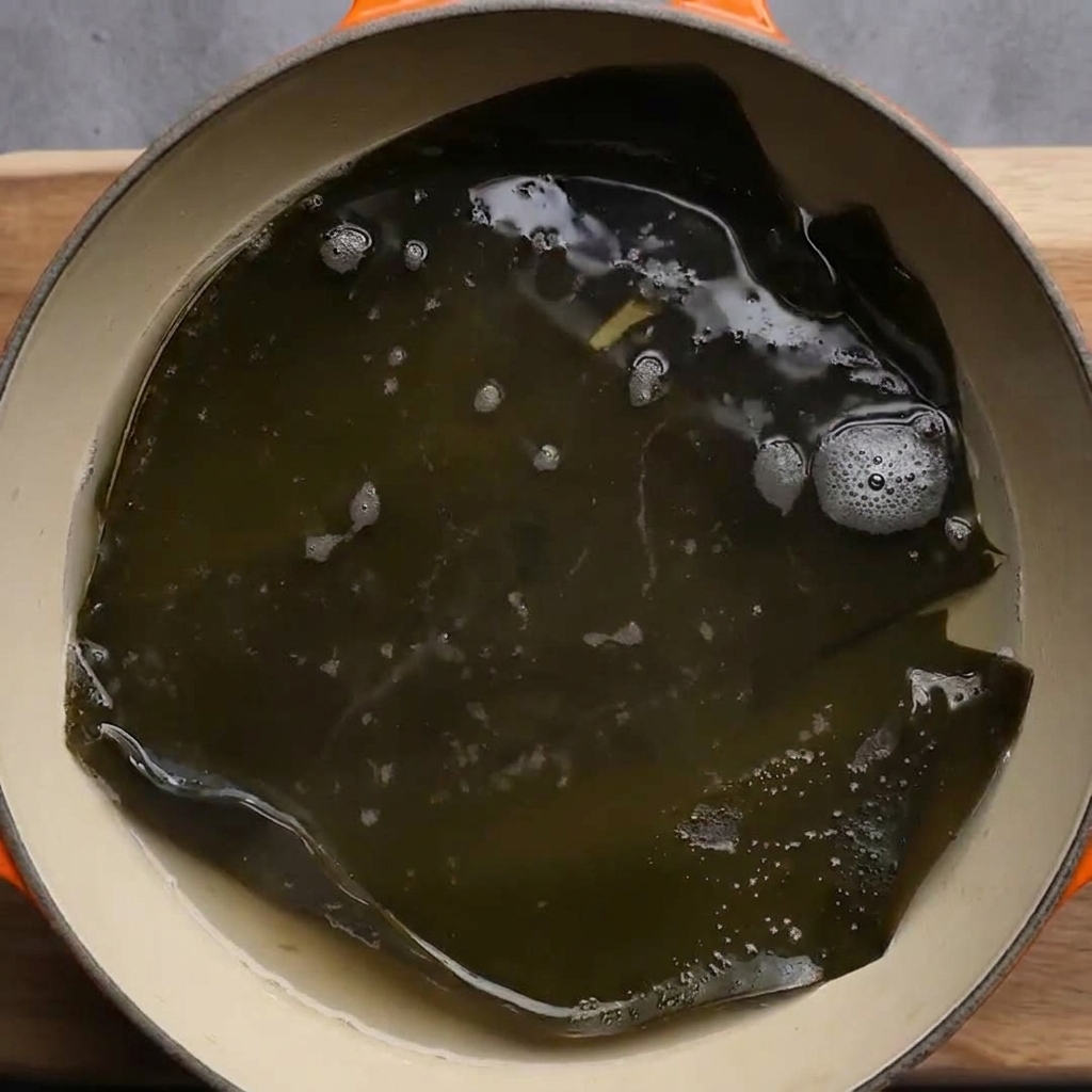Un pezzo di alga kombu scura che sobbolle in una pentola dacqua bollente.