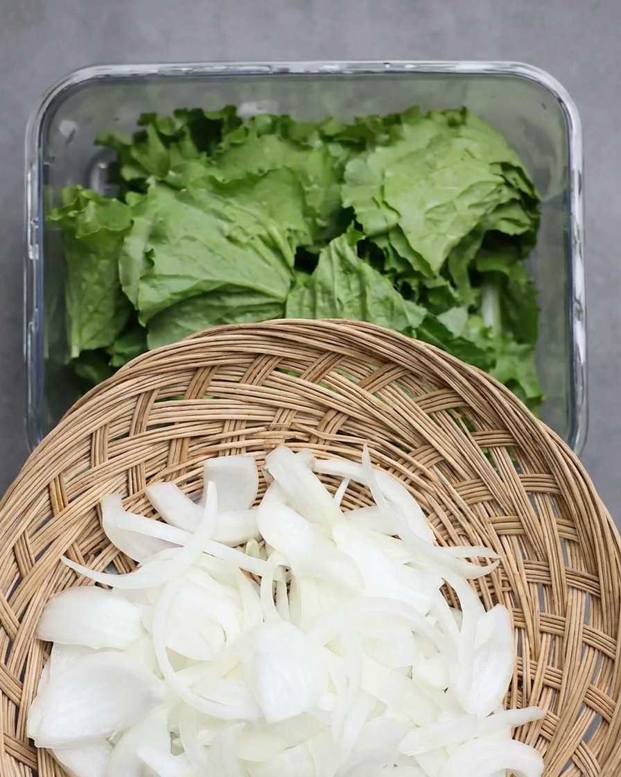 Cesto con cipolle bianche affettate sopra un contenitore di vetro pieno di lattuga fresca.