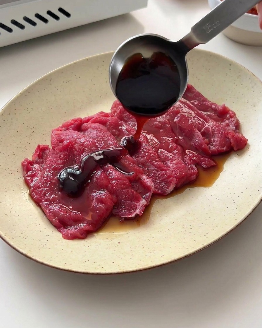 Salsa di soia e salsa dostriche versate da un cucchiaio dosatore sulle fette di manzo.