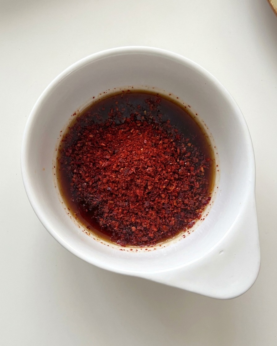 Una ciotolina bianca con salsa di soia e polvere di peperoncino rosso acceso.