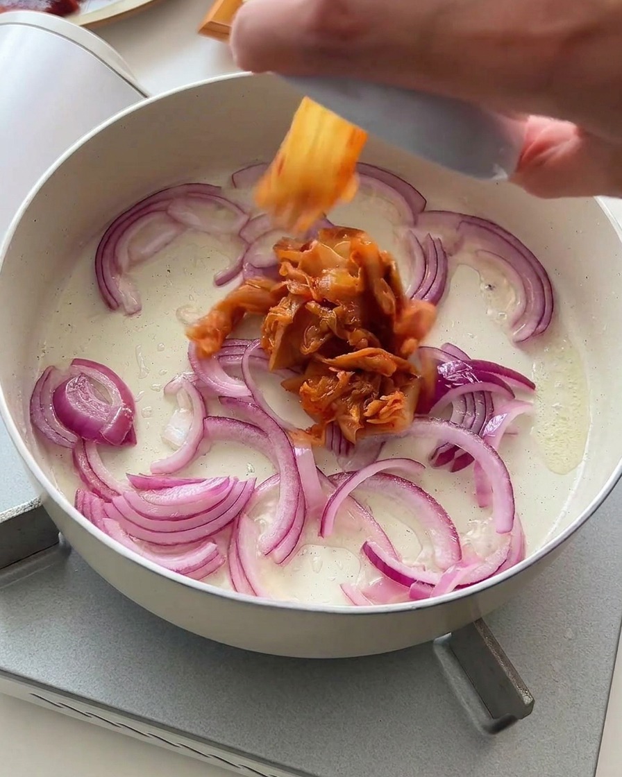 Kimchi tritato aggiunto alla padella con le cipolle rosse in olio.