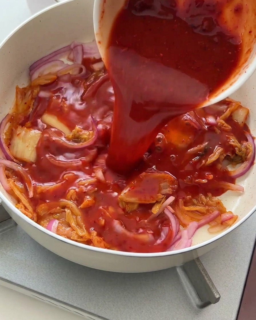 Salsa rossa vibrante versata da una ciotola bianca sopra il kimchi e le cipolle.