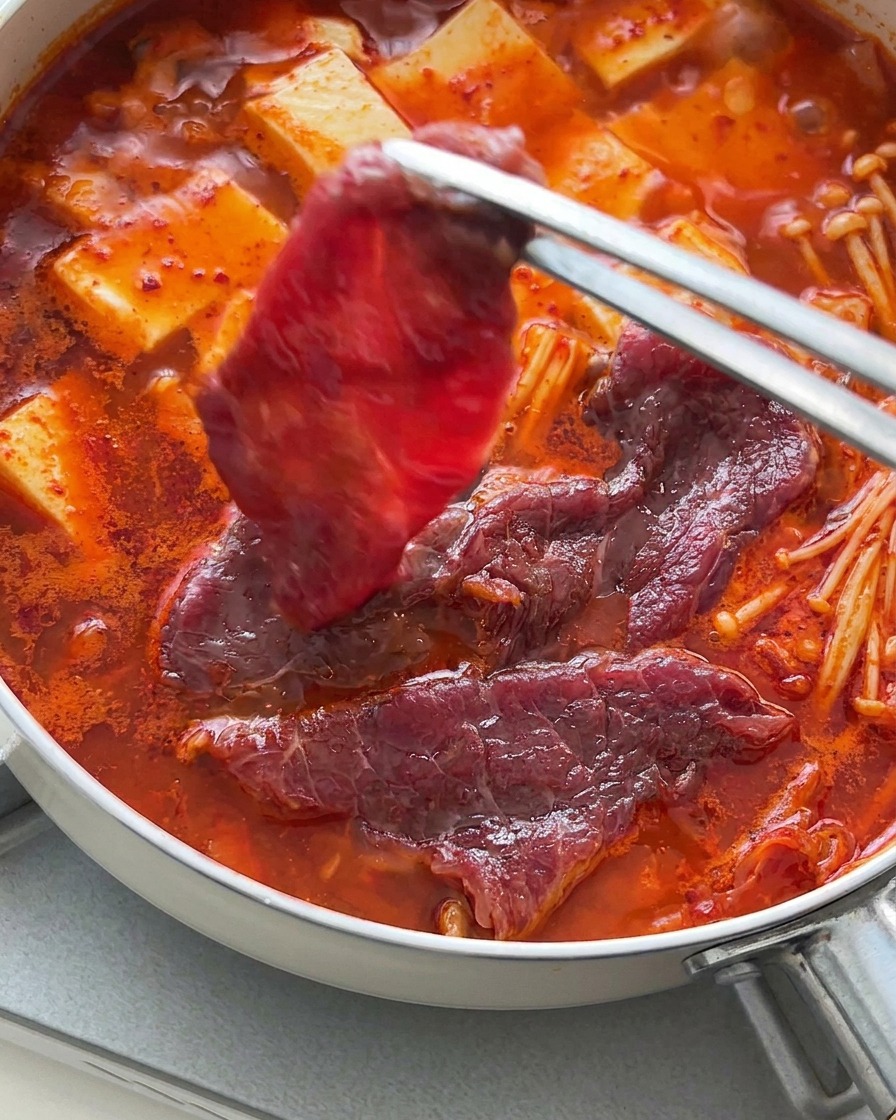 Pinze che adagiano fettine di manzo crudo sopra il tofu e il brodo bollente.