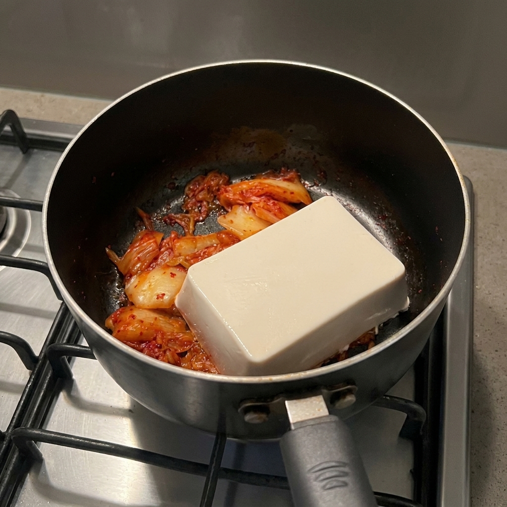 Un blocco rettangolare di tofu bianco appoggiato sopra il kimchi cotto in una pentola nera.