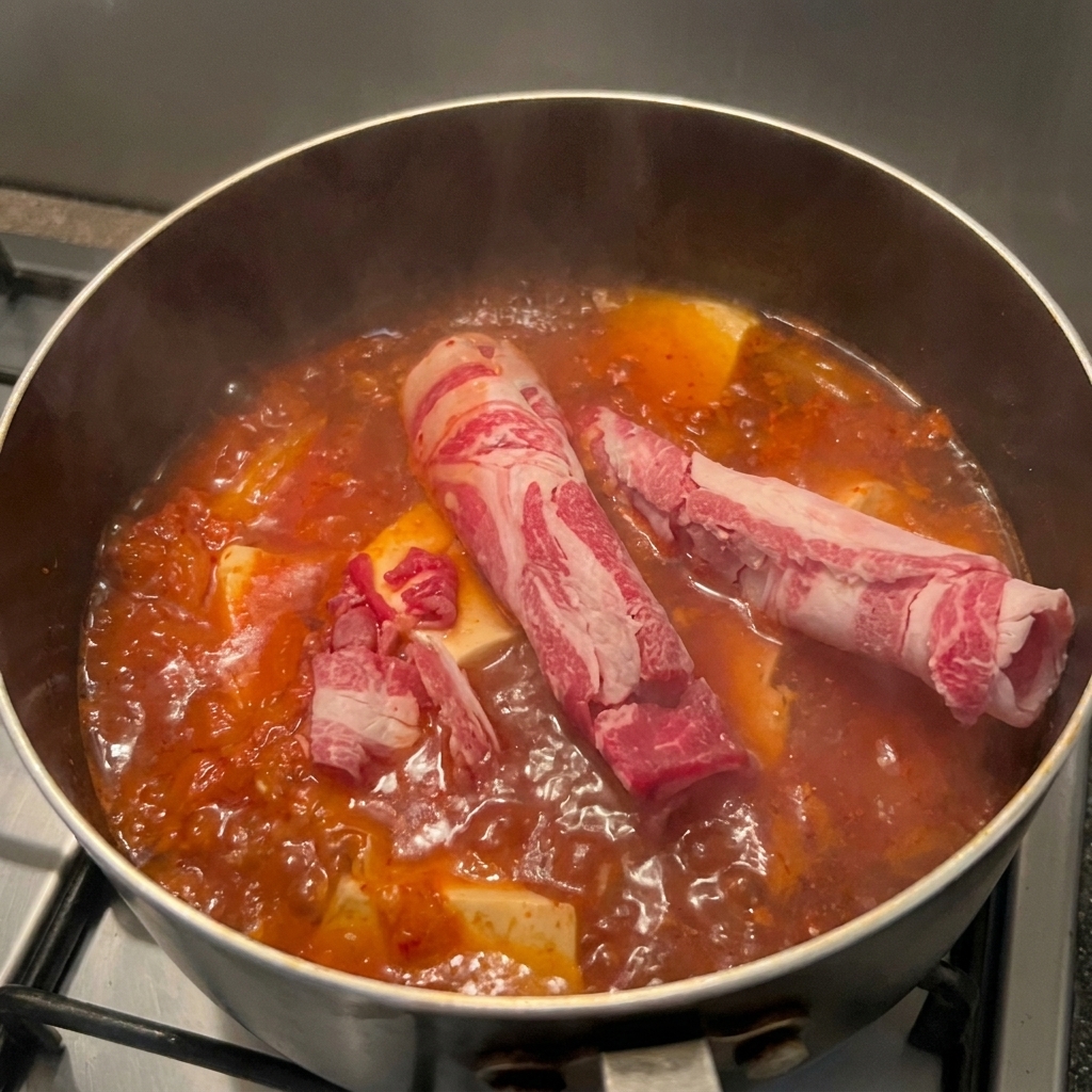 Fettine sottili di manzo marmorizzato messe in una pentola di zuppa di kimchi bollente con pezzi di tofu.