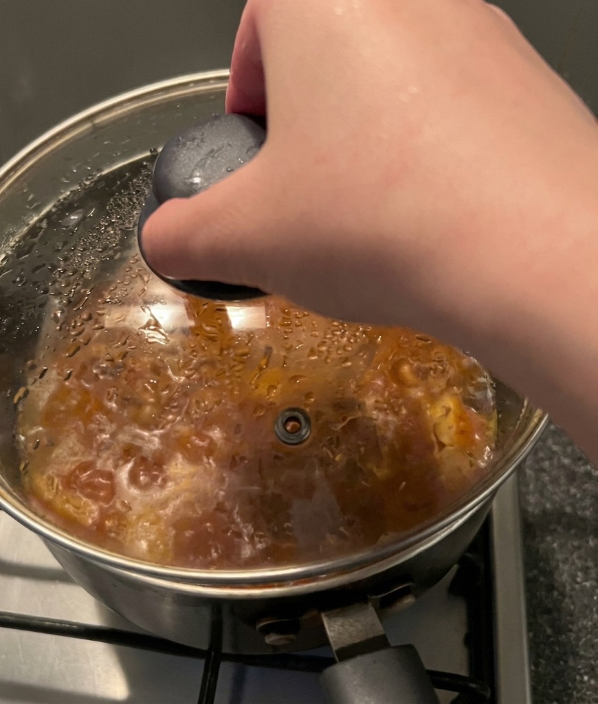 Una mano tiene il pomello nero di un coperchio di vetro e lo posiziona su una pentola fumante.