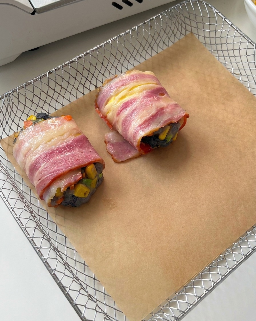 Involtini di gamberi e bacon disposti su carta forno allinterno del cestello della friggitrice ad aria.