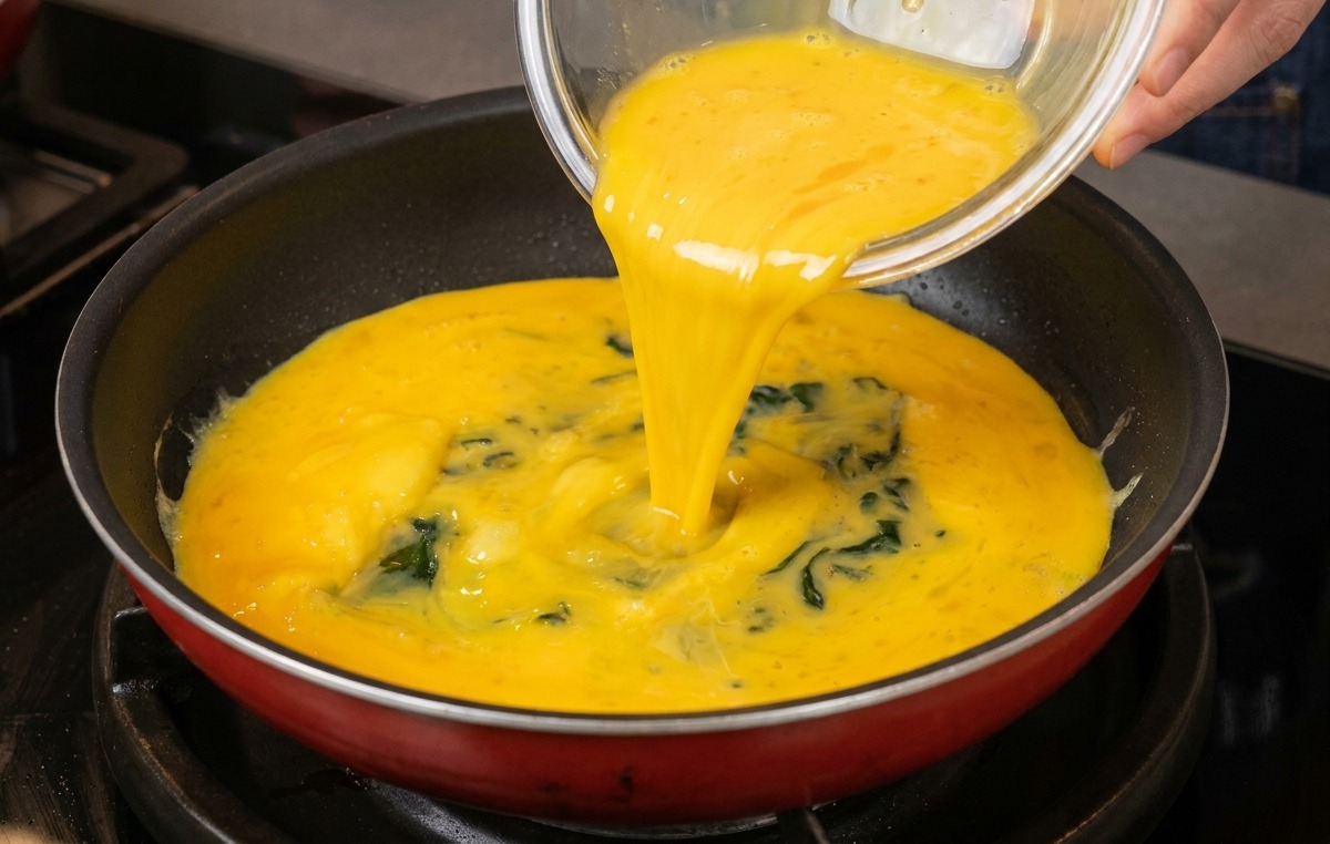Miscela di uova sbattute versata da una ciotola di vetro in una padella pulita.