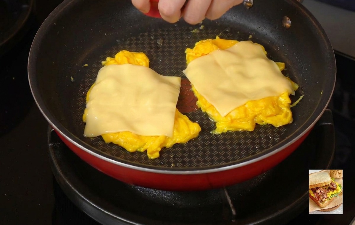 Una persona che mette un coperchio rosso su una padella per intrappolare il vapore e sciogliere il formaggio sopra le uova strapazzate.