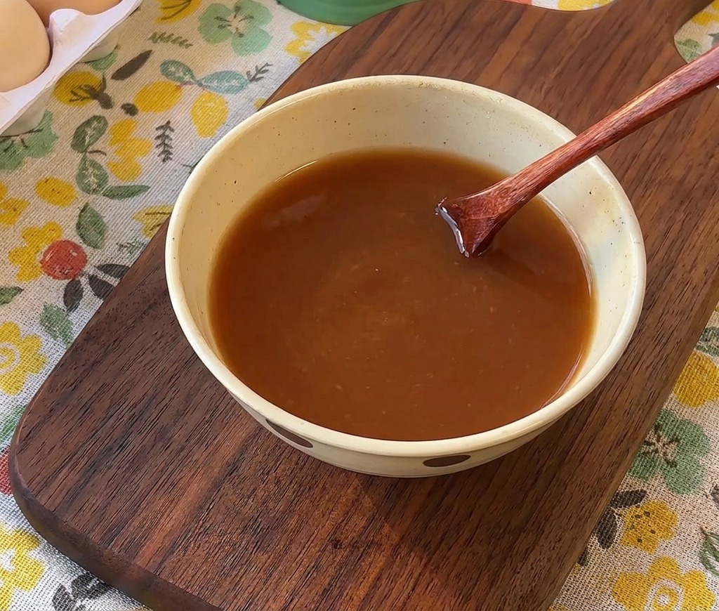 Un cucchiaio di legno che mescola la salsa marrone in una ciotola di ceramica.