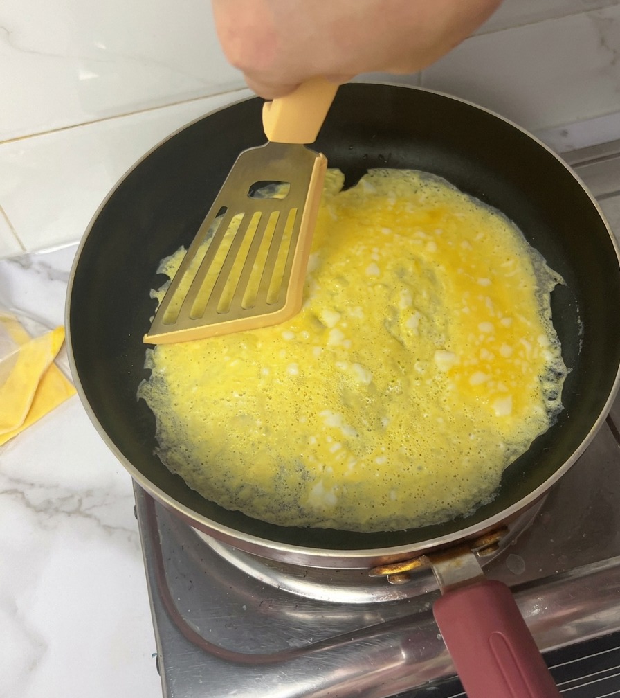 Una mano usa una spatola gialla per tagliare una sottile frittata in quattro sezioni uguali in una padella nera.