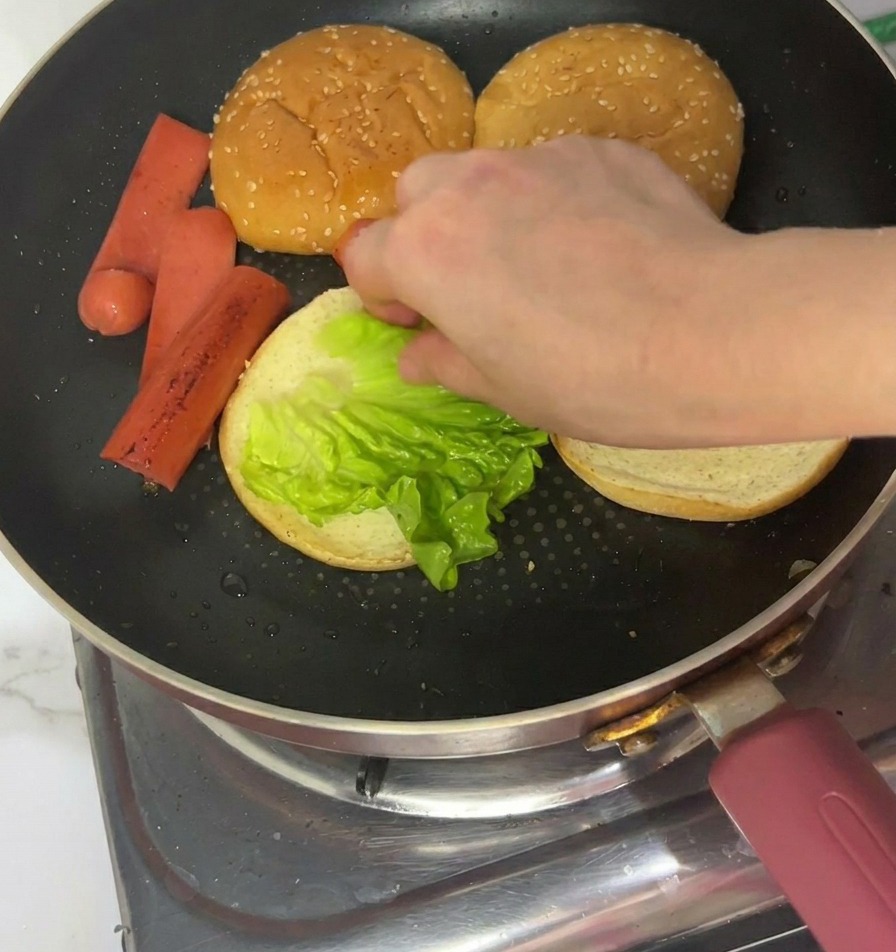 Una mano posiziona una foglia di lattuga verde brillante sul lato tostato di un panino in padella.