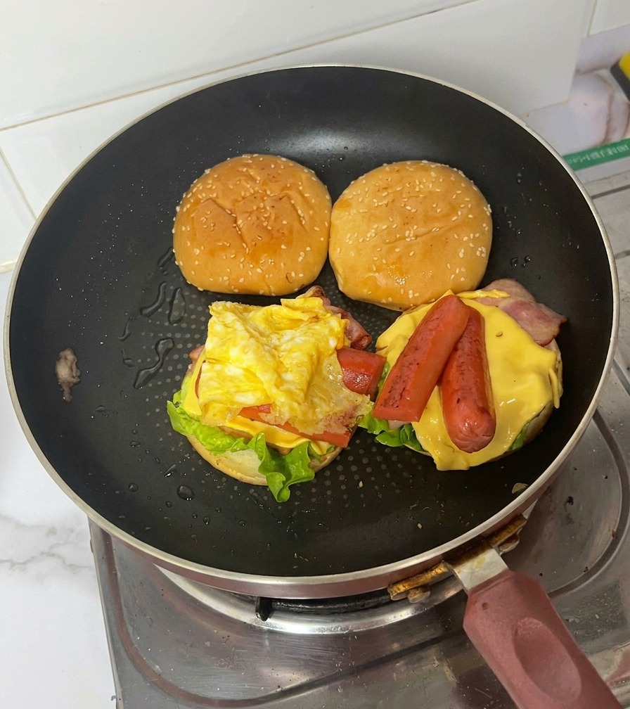 Un burger completo in padella che mostra la frittata ripiegata sopra i wurstel, il formaggio, il bacon e la lattuga.