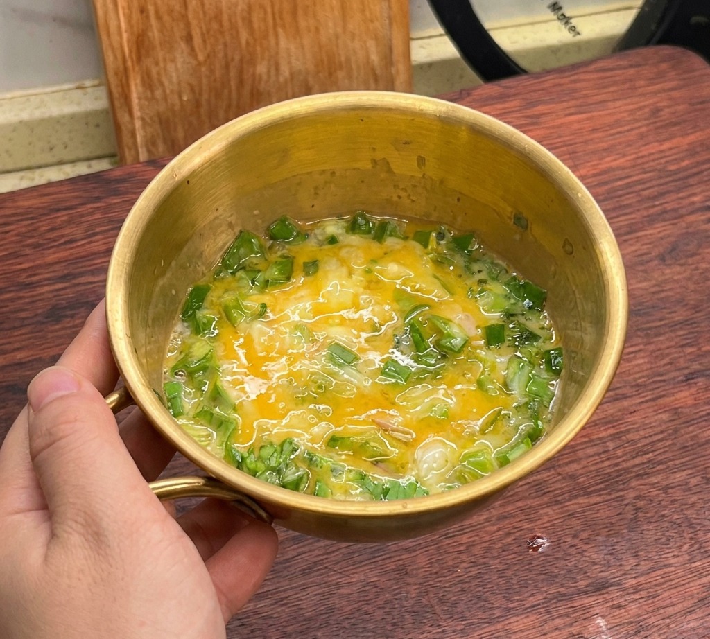 Miscela di uova sbattute e lattuga verde combinata in una ciotola dorata.
