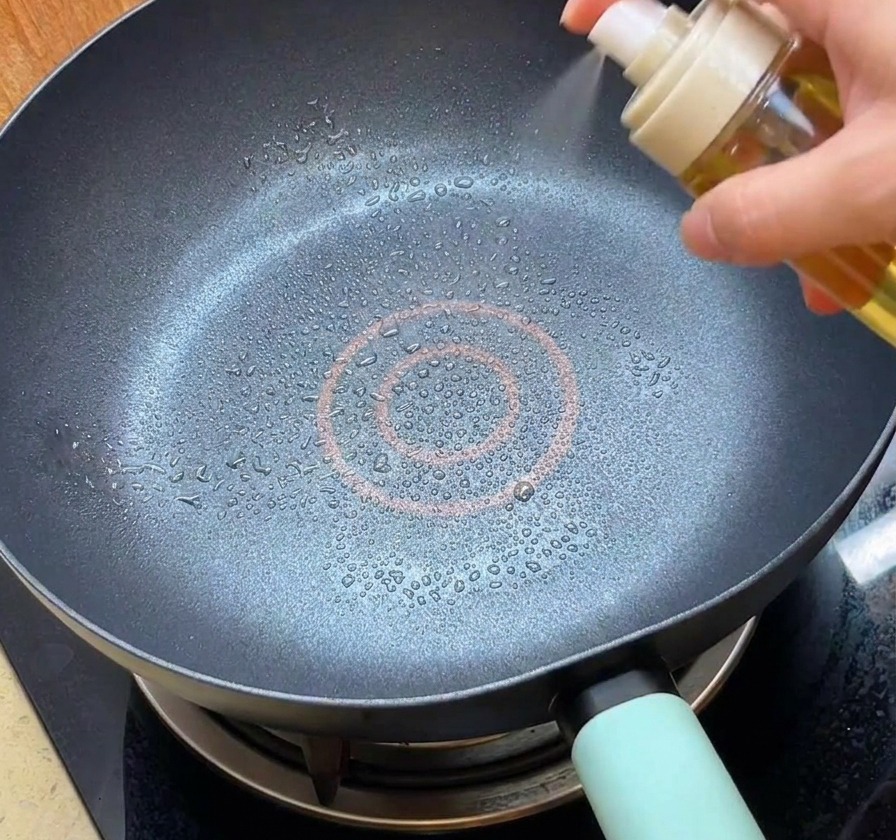 Una persona nebulizza olio spray in una padella antiaderente nera pulita.