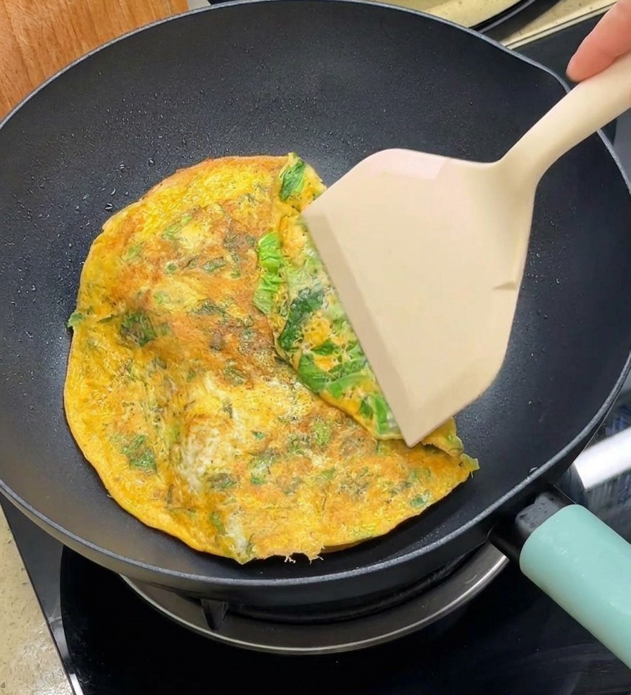 Una spatola ripiega i bordi di una frittata tonda sopra le due metà del panino in padella.