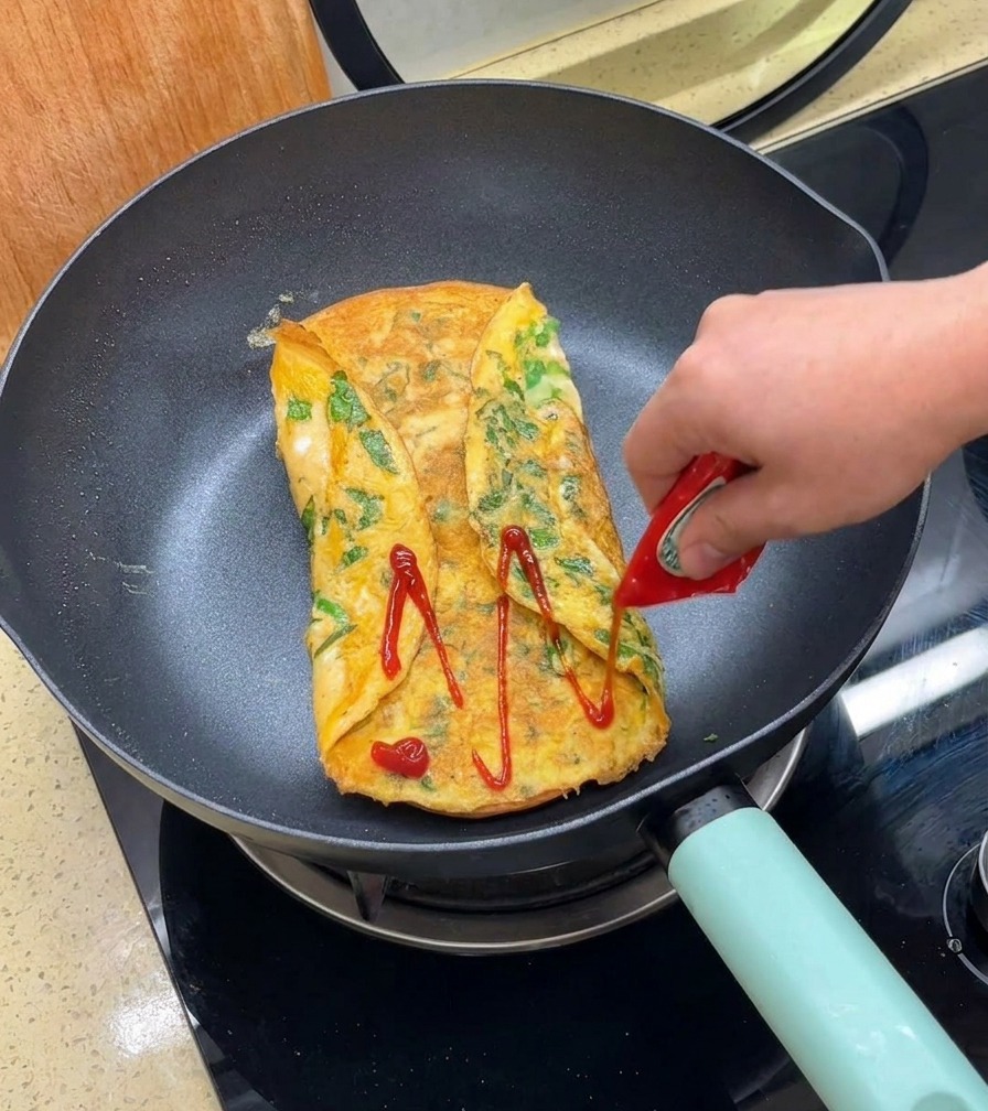 Ketchup rosso versato sopra una frittata ripiegata e dorata in una padella.