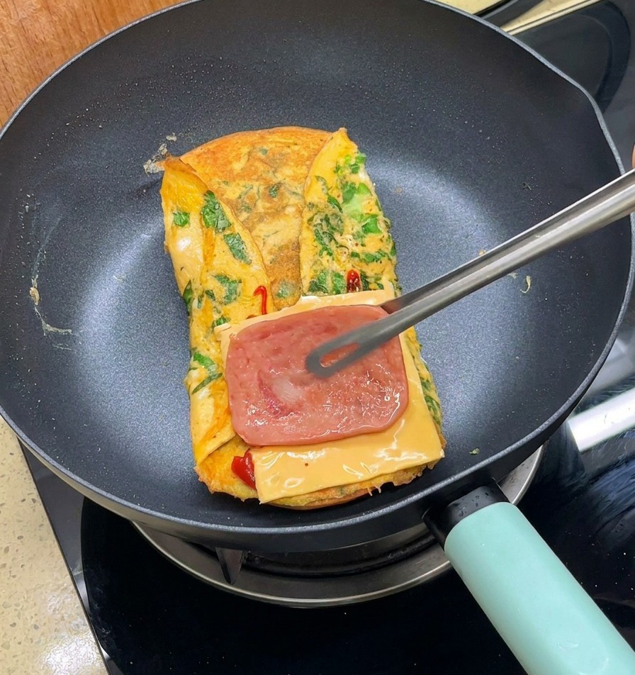 Pinze metalliche che posizionano la pancetta cotta sopra il formaggio in padella.