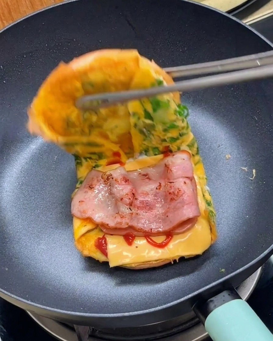 Pinze che chiudono a metà il sandwich di uova e pane per completare il burger in padella.