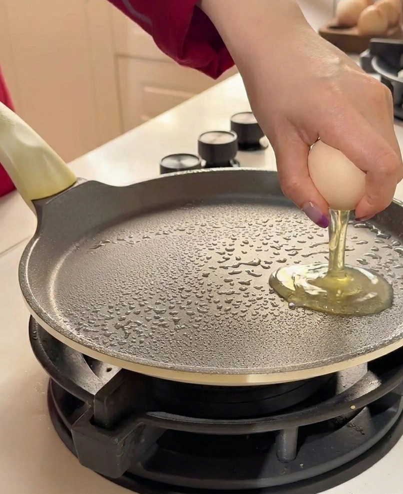 Due uova fresche vengono rotte a mano su una padella piatta unta.