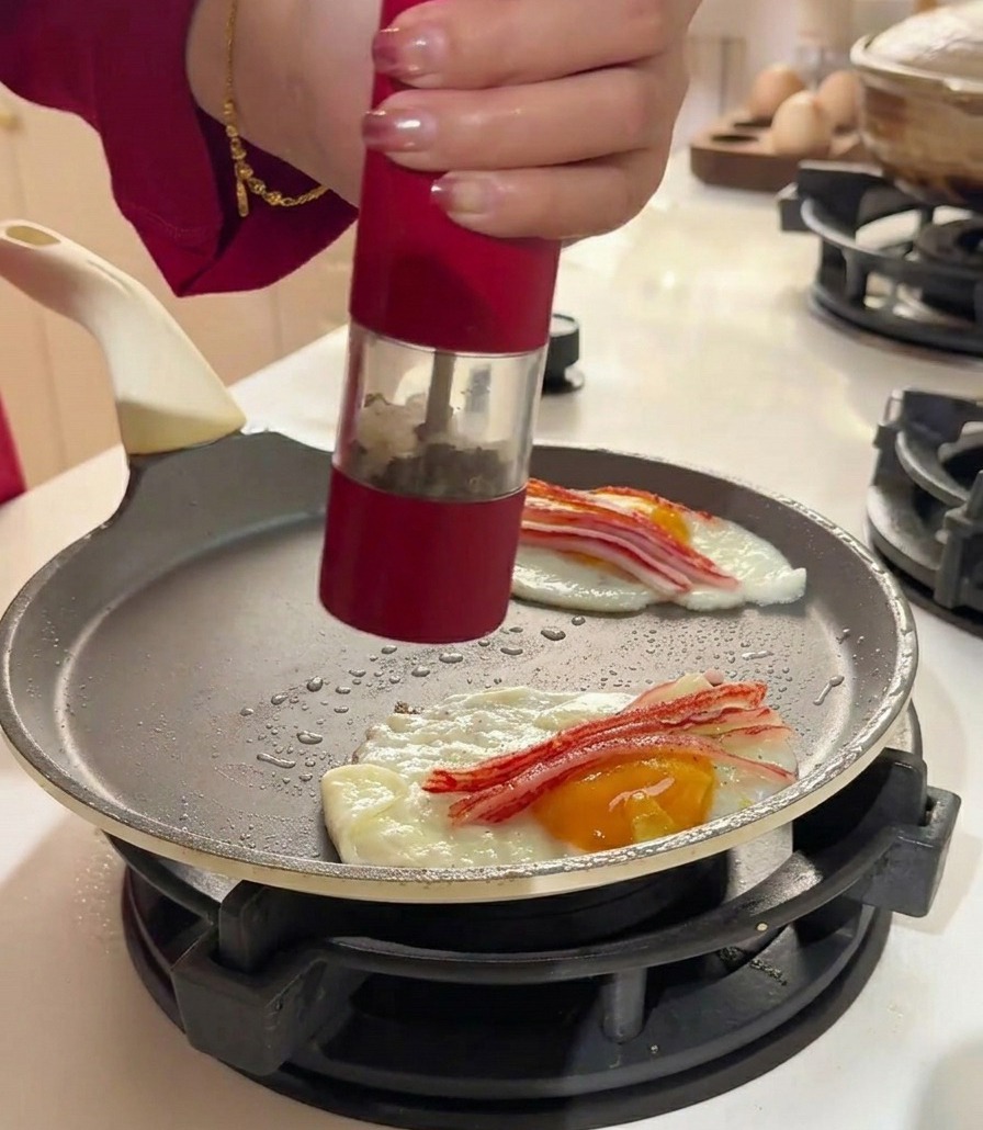 Un macinapepe rosso condisce uova e surimi in una padella piatta.