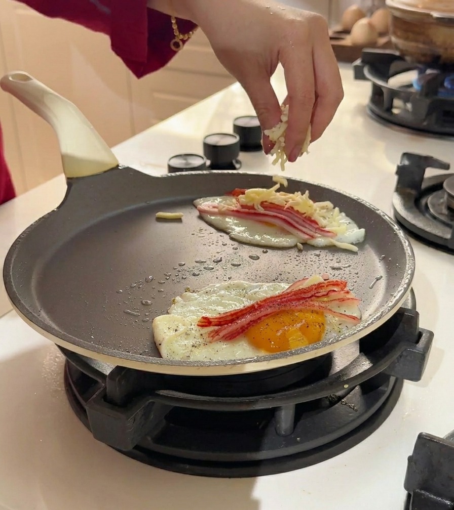 Formaggio a julienne cosparso sopra uova e surimi in padella.