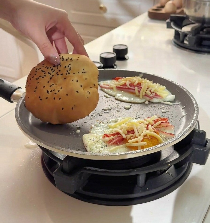 Mano che posiziona un panino soffice dorato con semi di sesamo sopra un uovo con surimi e formaggio fuso.