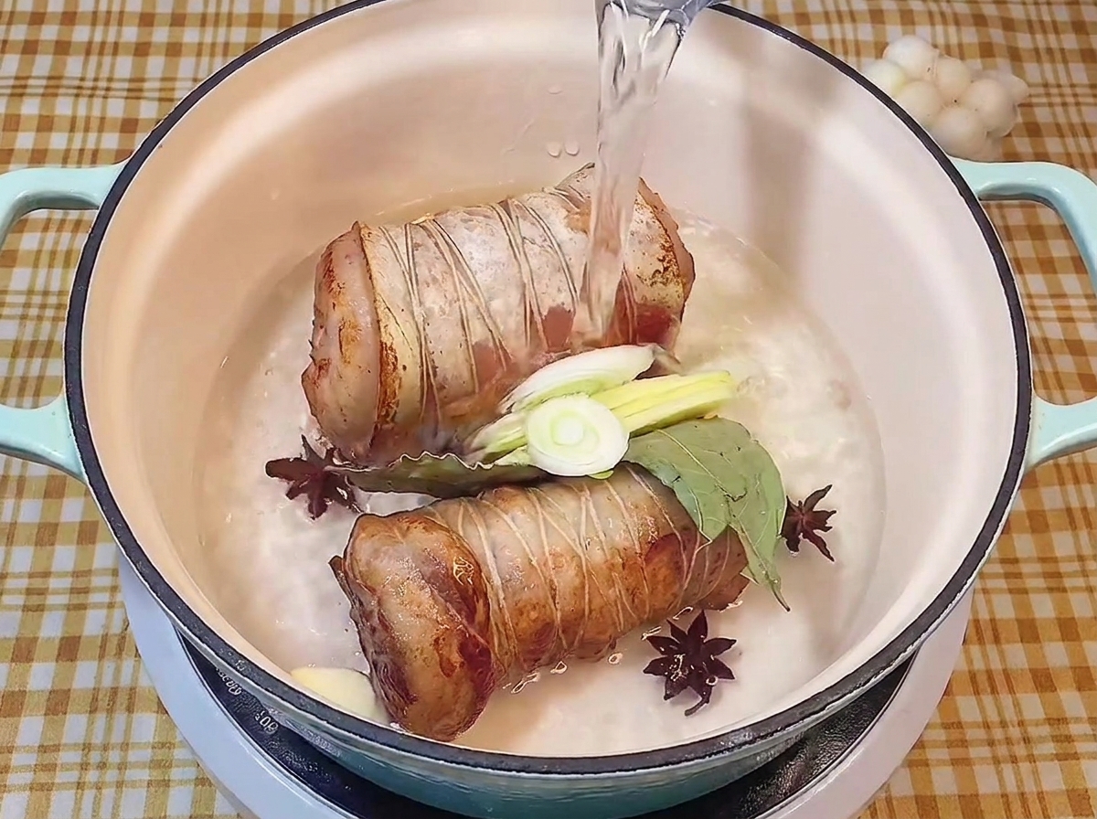 Versare acqua pulita in una pentola con i rotoli di maiale, erbe aromatiche e spezie.