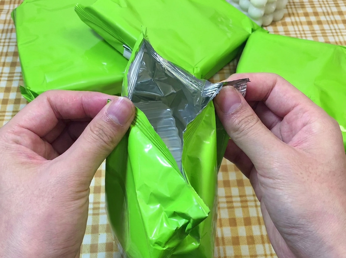 Mani che aprono un pacchetto verde di ramen istantaneo mostrando il contenuto.