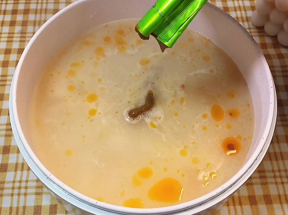 Pasta di condimento scura versata in una pentola con brodo lattiginoso in ebollizione.