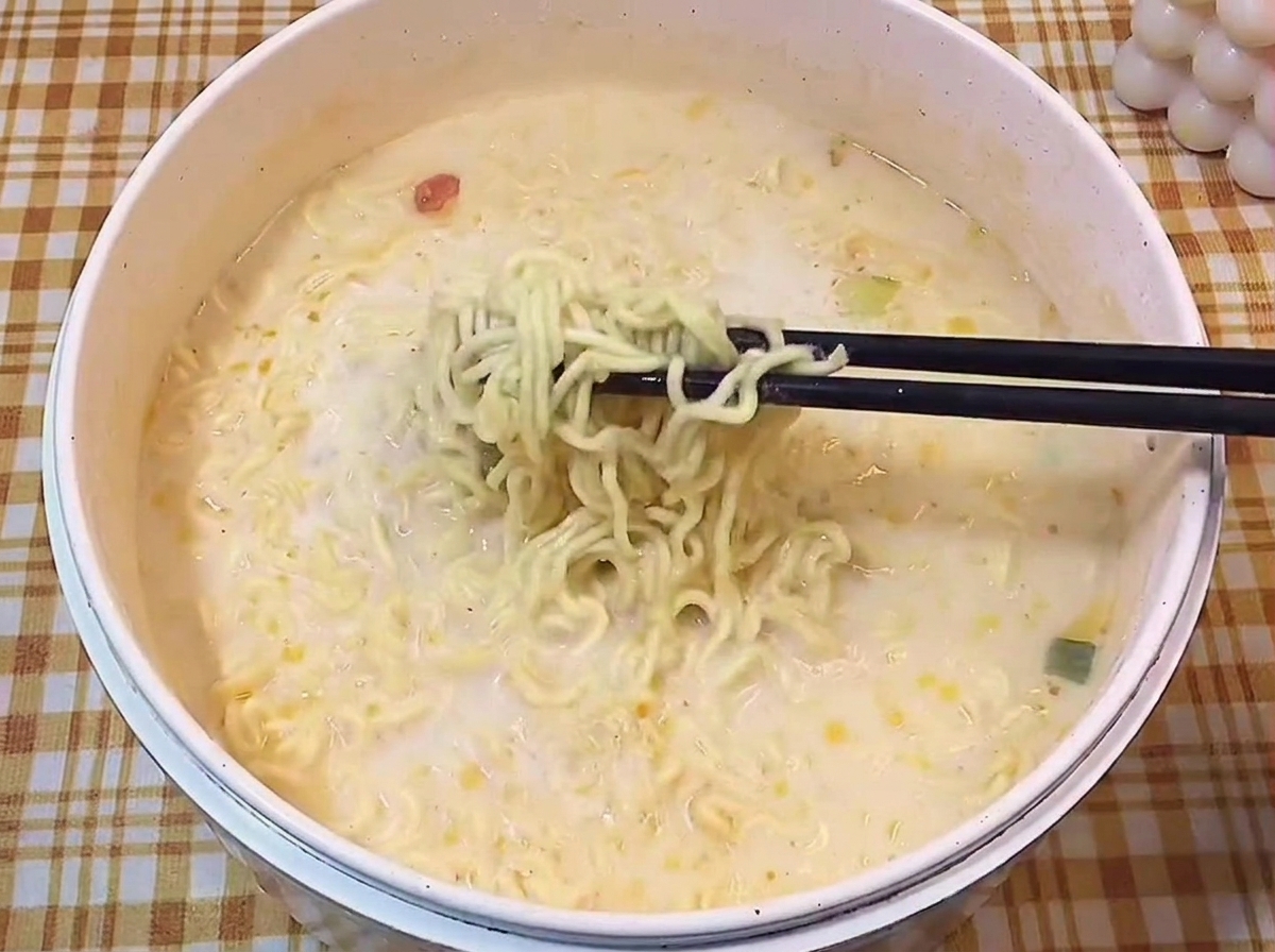Bacchette nere che sollevano i noodles ondulati dal brodo cremoso.