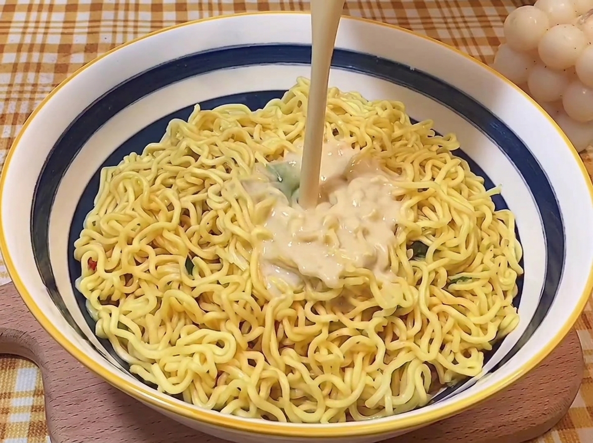 Un getto di brodo tonkotsu cremoso versato sopra i noodles in una ciotola.