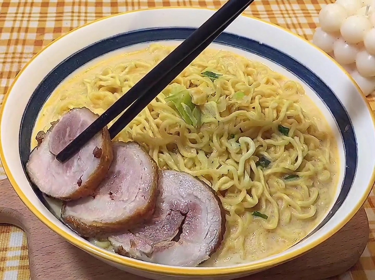 Bacchette che posizionano con cura le fette di pancetta brasata in una ciotola di ramen.