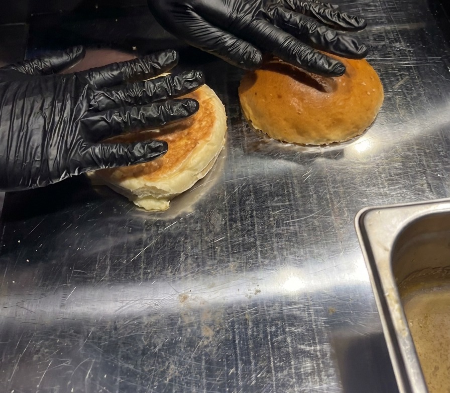 Due panini da burger vengono premuti a mano su una piastra calda per tostare la parte interna.