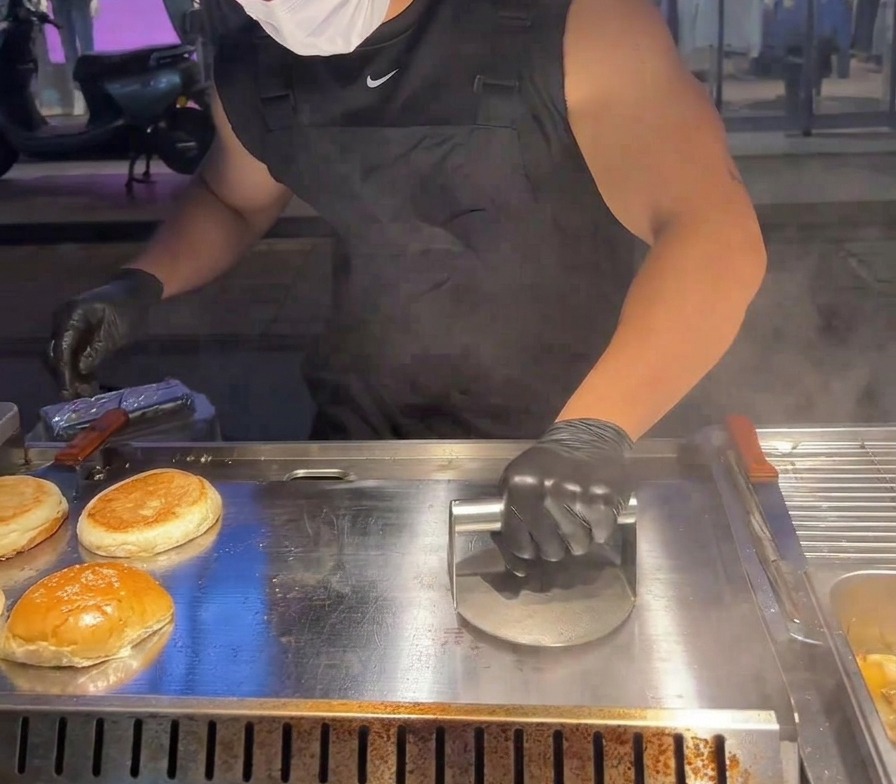 Una pressa metallica pesante viene usata per schiacciare la carne contro la piastra rovente.