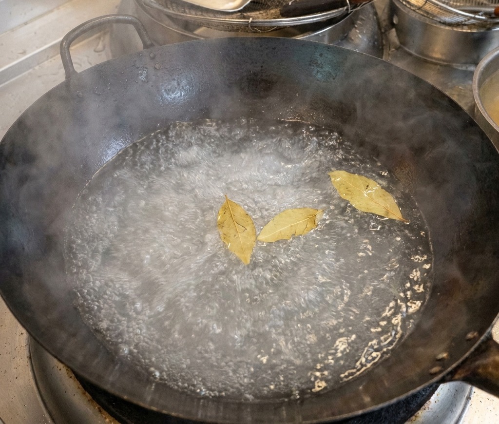 Un grande wok nero pieno dacqua bollente con tre foglie di alloro che galleggiano in superficie.