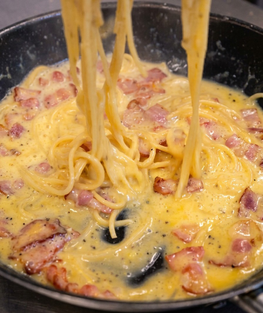 Spaghetti saltati in padella, con la salsa che si trasforma in un rivestimento denso, cremoso e giallo paglierino sulla pasta.