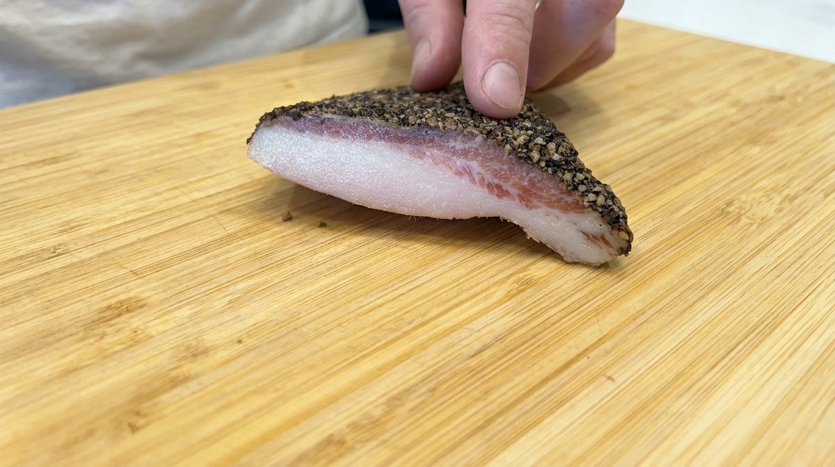 Un pezzo di guanciale pepato su un tagliere di legno.