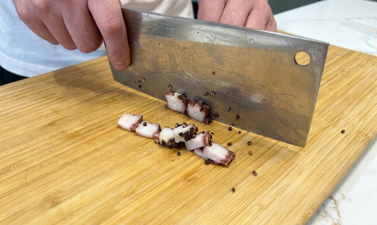 Taglio del guanciale a cubetti con un coltello su un tagliere.