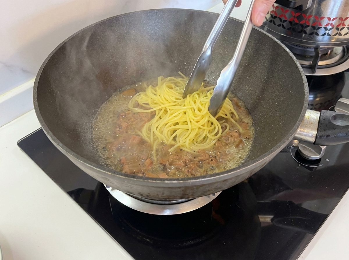 Pinze che spostano gli spaghetti dalla pentola alla padella.