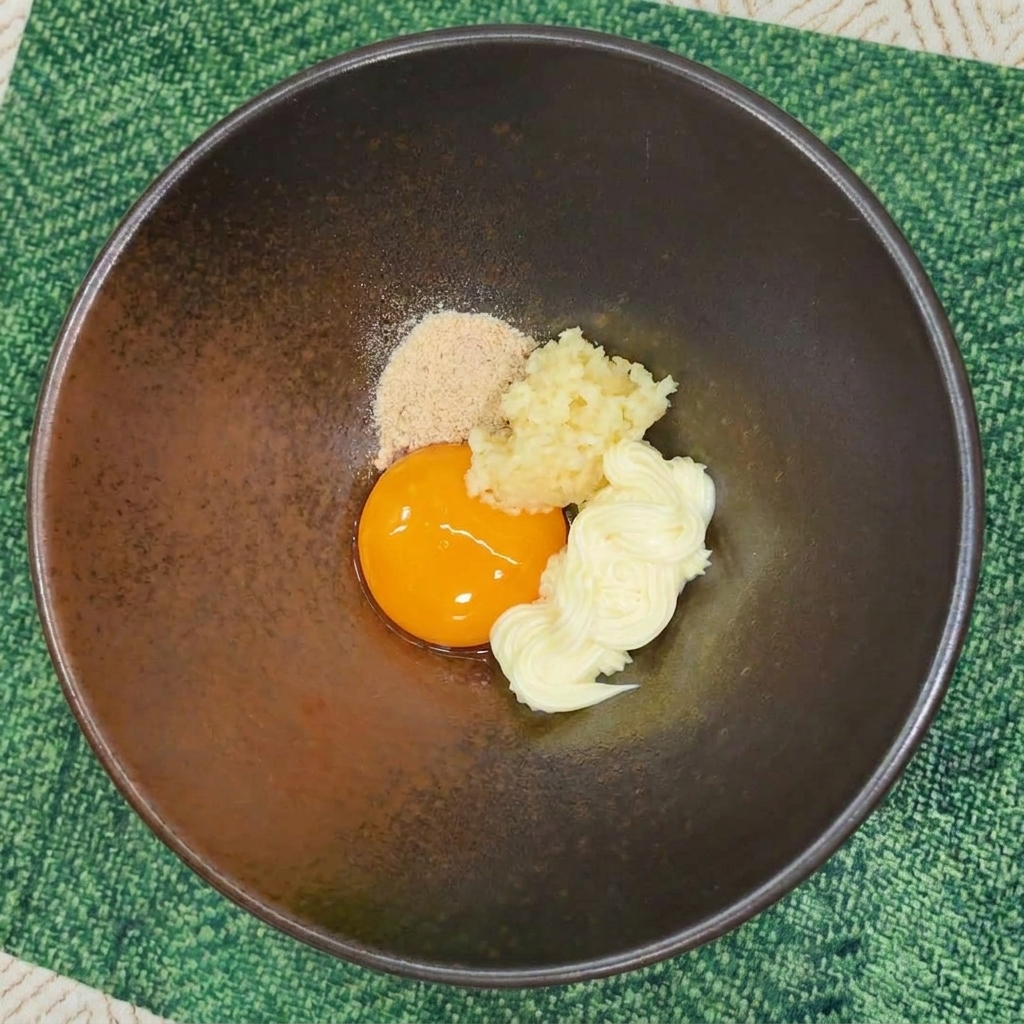 Polvere di condimento per ramen istantaneo aggiunta a una ciotola con tuorlo, aglio e maionese.