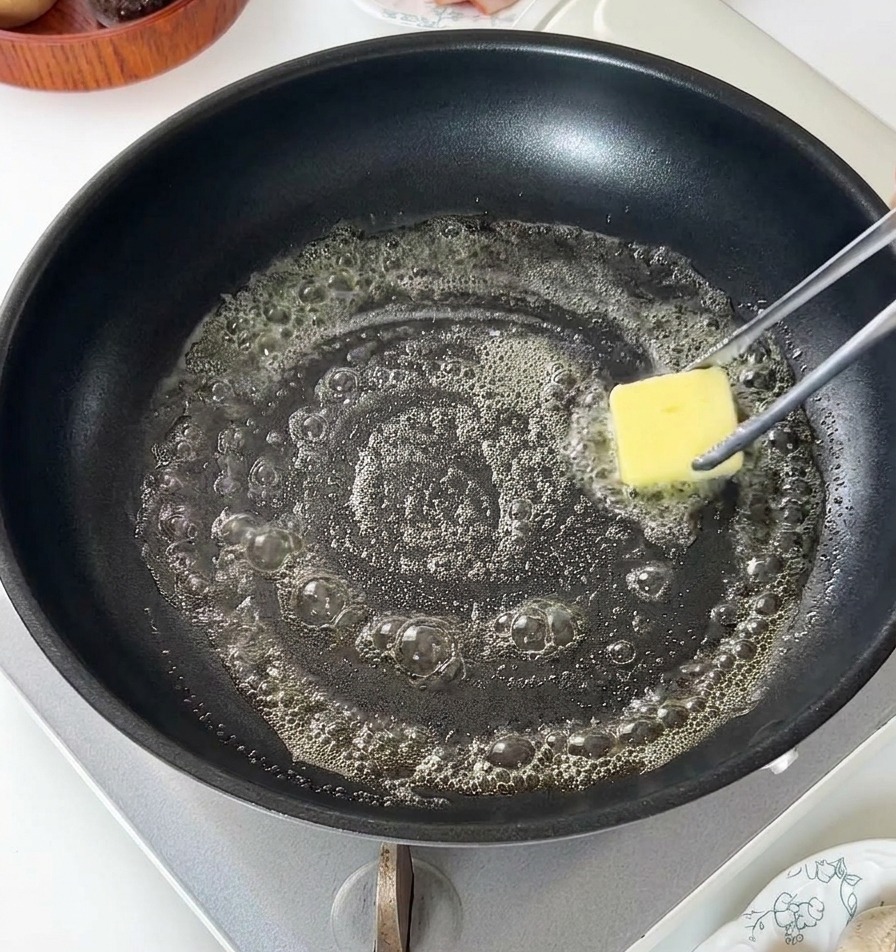 Un panetto di burro giallo che si scioglie e sfrigola in una padella antiaderente nera.