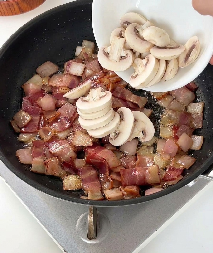 Una persona versa funghi bianchi affettati in una padella con pancetta rosolata e cipolle.