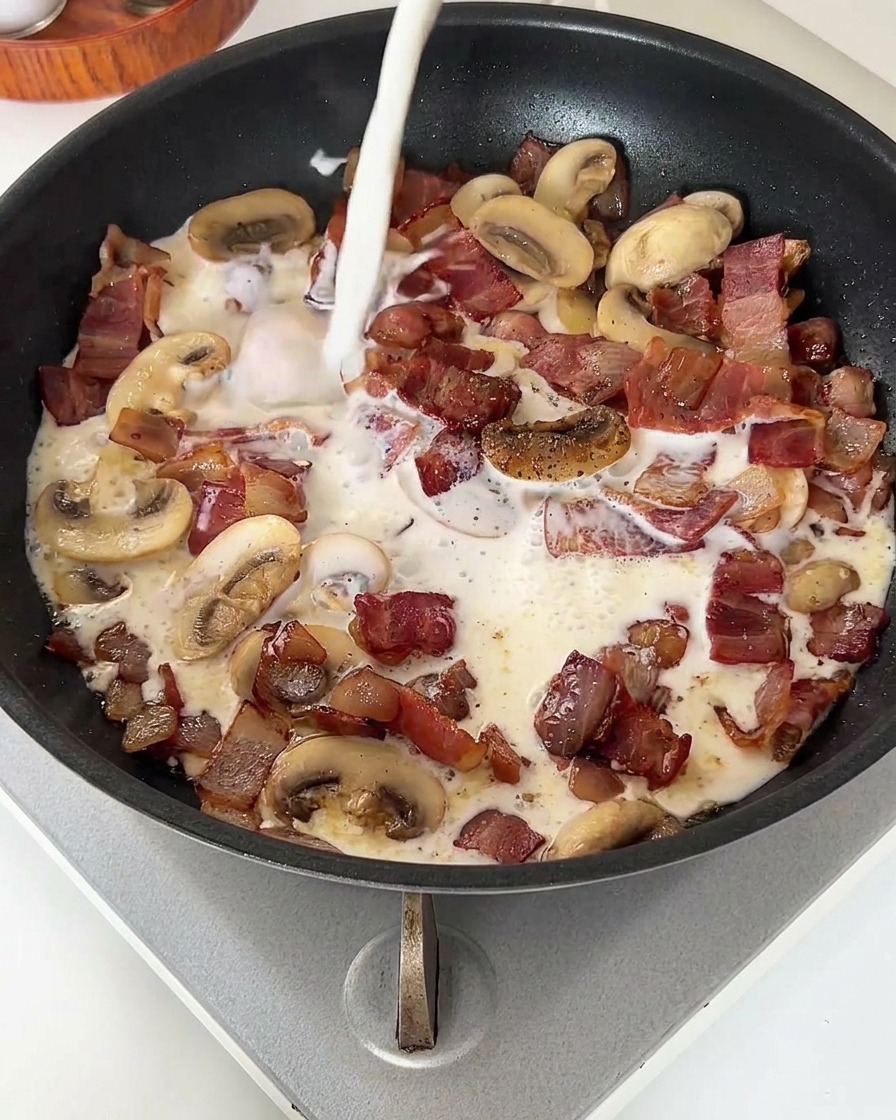 Un filo di latte bianco versato in una padella con pancetta e funghi cotti.