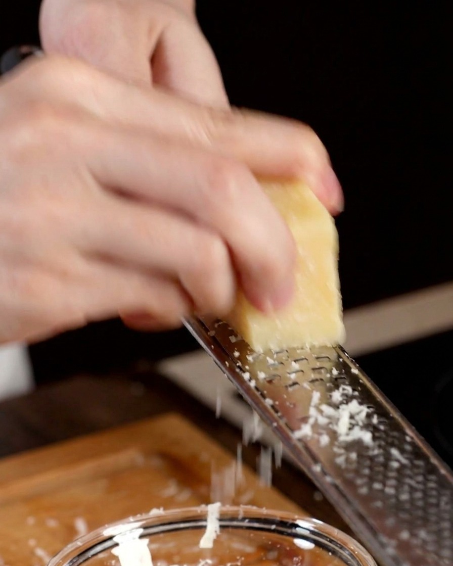 Una mano che usa una grattugia per ridurre un pezzo di Parmigiano in una ciotola.
