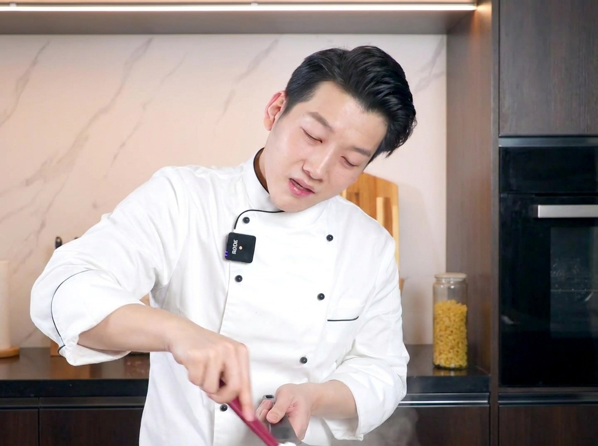 Uno chef che mescola la pasta cremosa con una spatola rossa, amalgamando la salsa alluovo.