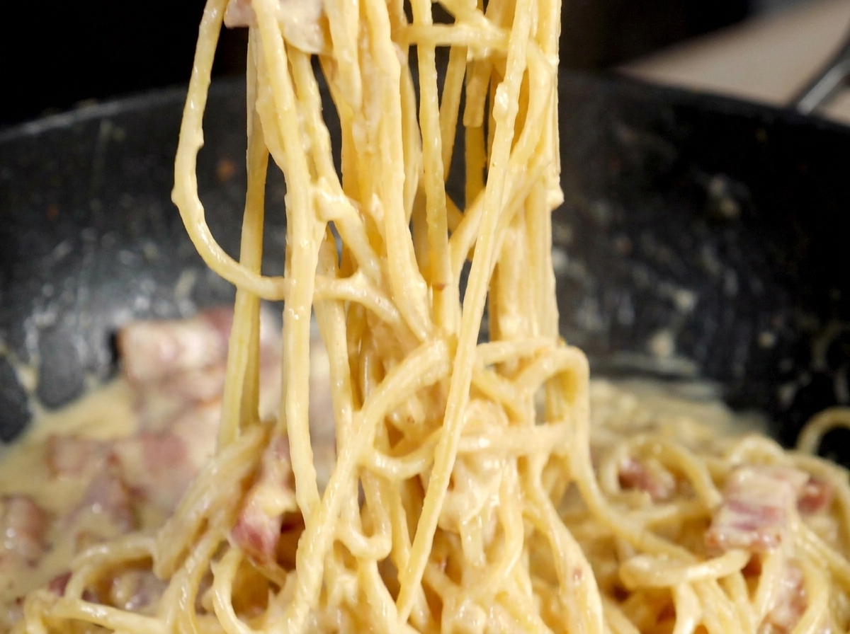 Un macinapepe in metallo che spolvera pepe nero su una padella di pasta tipo carbonara.