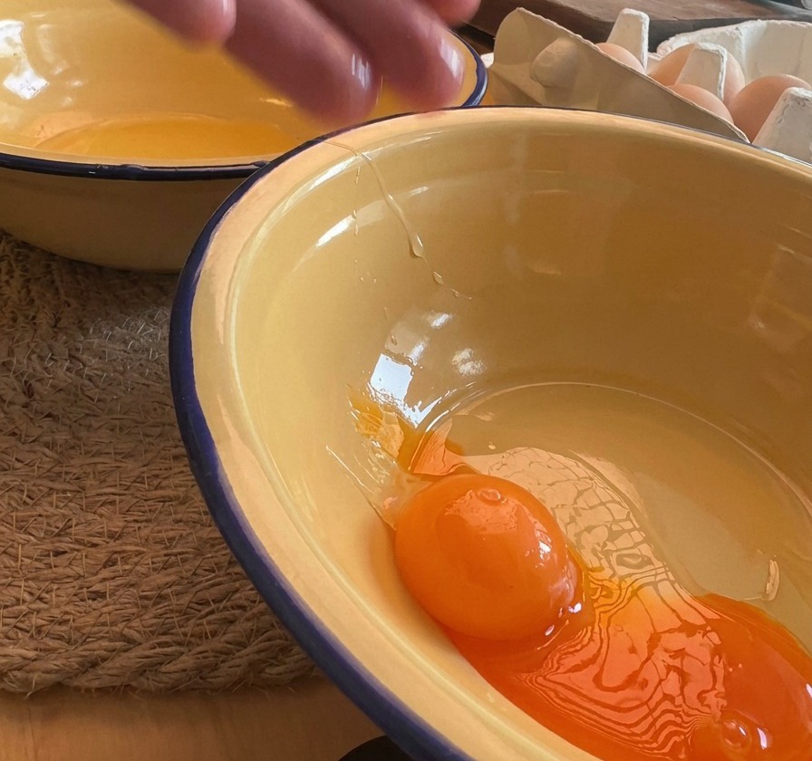 Dettaglio di un tuorlo duovo arancione brillante che cade in una ciotola smaltata gialla.